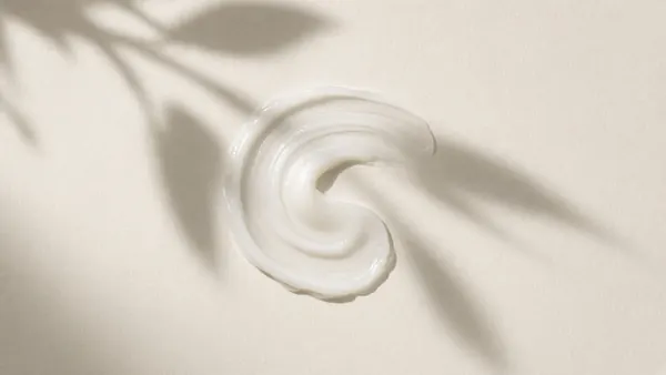 A swirl of lightweight white lotion under soft leaf shadows