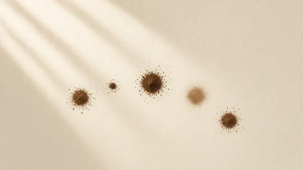 Small dots of brown pigment scattered across cream paper in soft light